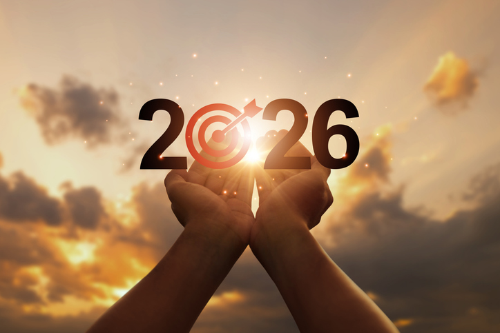 Hands lifting “2026” with a bullseye in the zero, set against a sunrise—symbolizing renewed nonprofit mission, goal setting, vision, and growth in the new year.